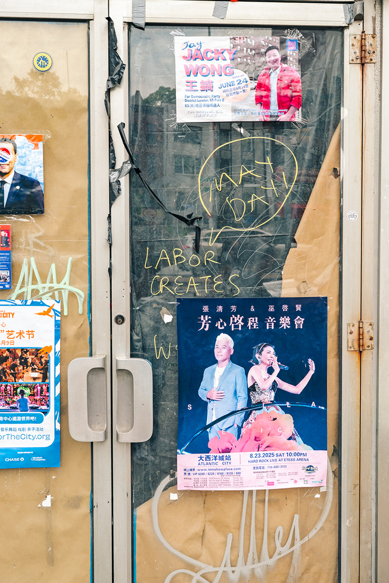 Weathered Chinatown storefront door with posters and the yellow words Labor Creates written on the glass