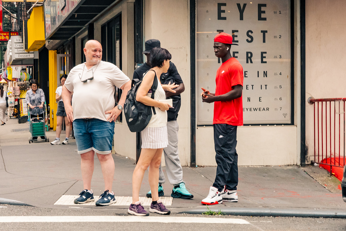 People talking outside an eyewear shop as a man in red stands beside a large eye-test chart