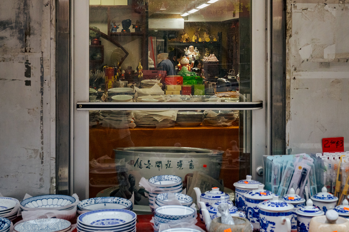 Blue-and-white bowls and teaware displayed outside a shop with two workers visible through the window