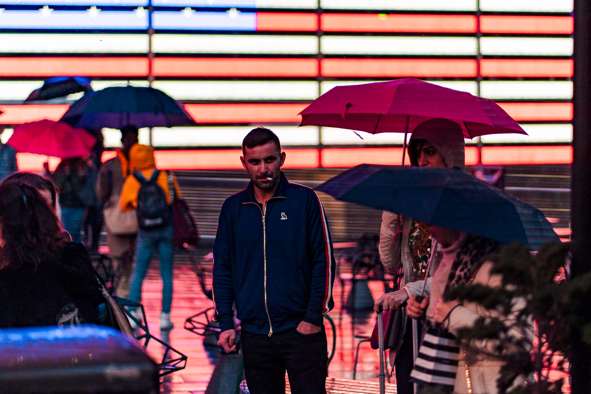 Person in a dark jacket among pedestrians carrying umbrellas, against bright red-and-white illuminated stripes.