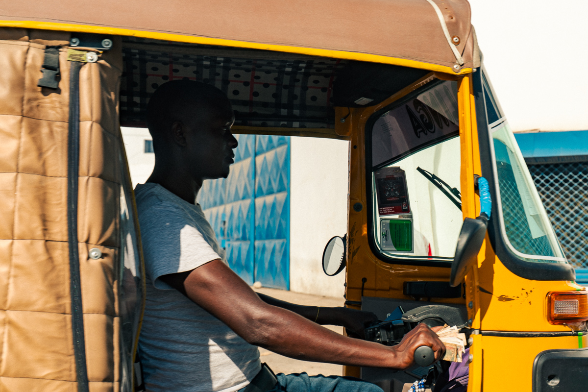 Driver seen through the open side of a yellow tuk-tuk.