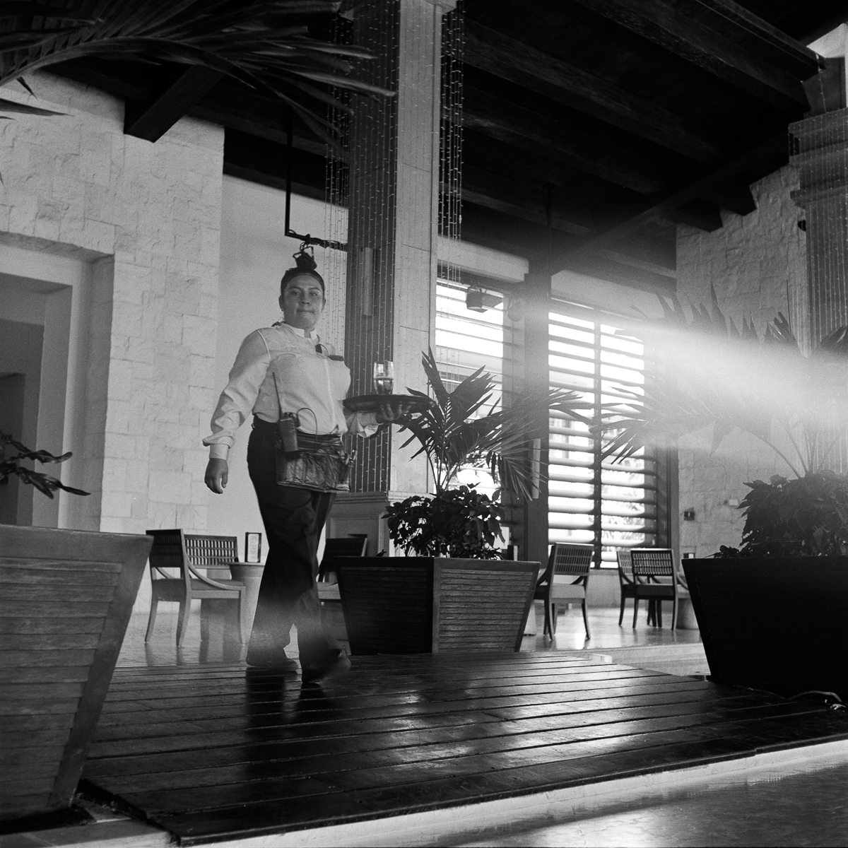 Woman holding a drink beside a column and looking toward the camera, with a light leak along the edge of the photograph.