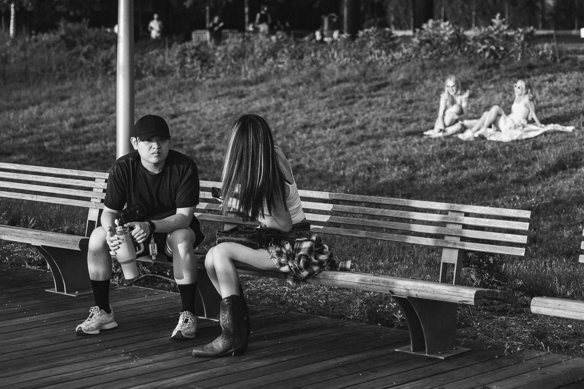 Two people sitting on a wooden bench, with two more people on the grass behind them