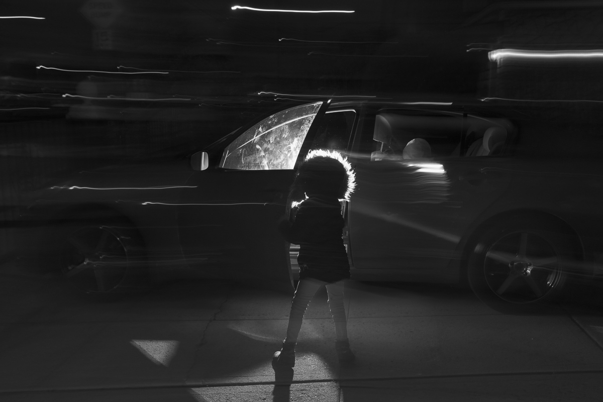 A child silhouetted against a car, with streaks of light and motion blur in black and white