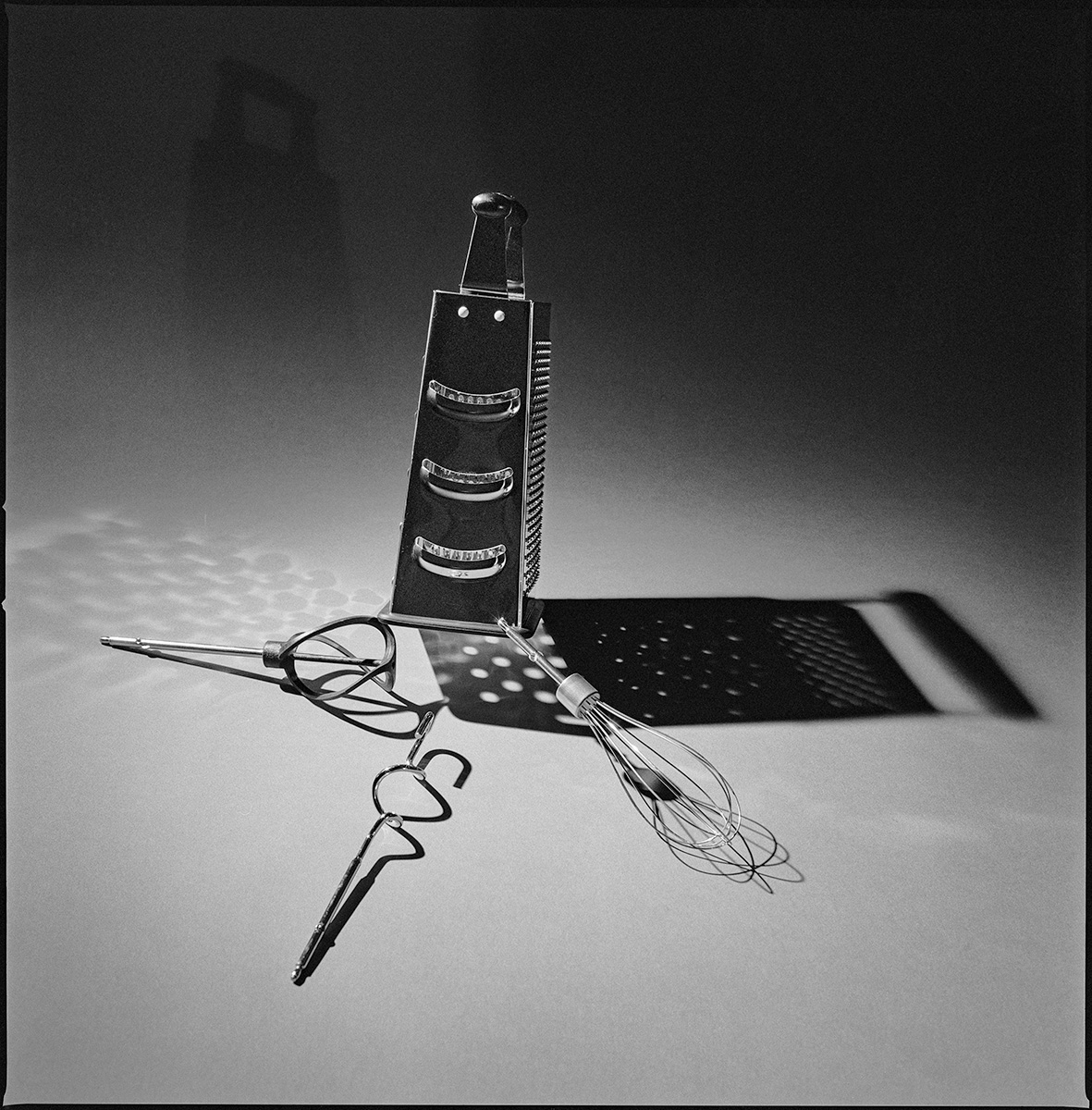 Still life photograph of kitchen tools including a grater and whisks